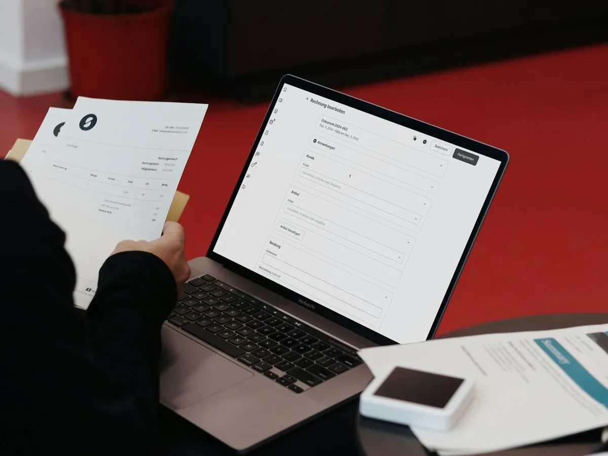 Person processing invoices on a laptop with paper invoices in hand