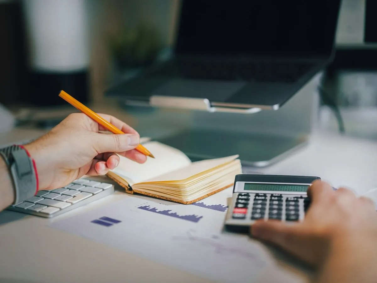 Person writing in a notebook while using a calculator at a desk