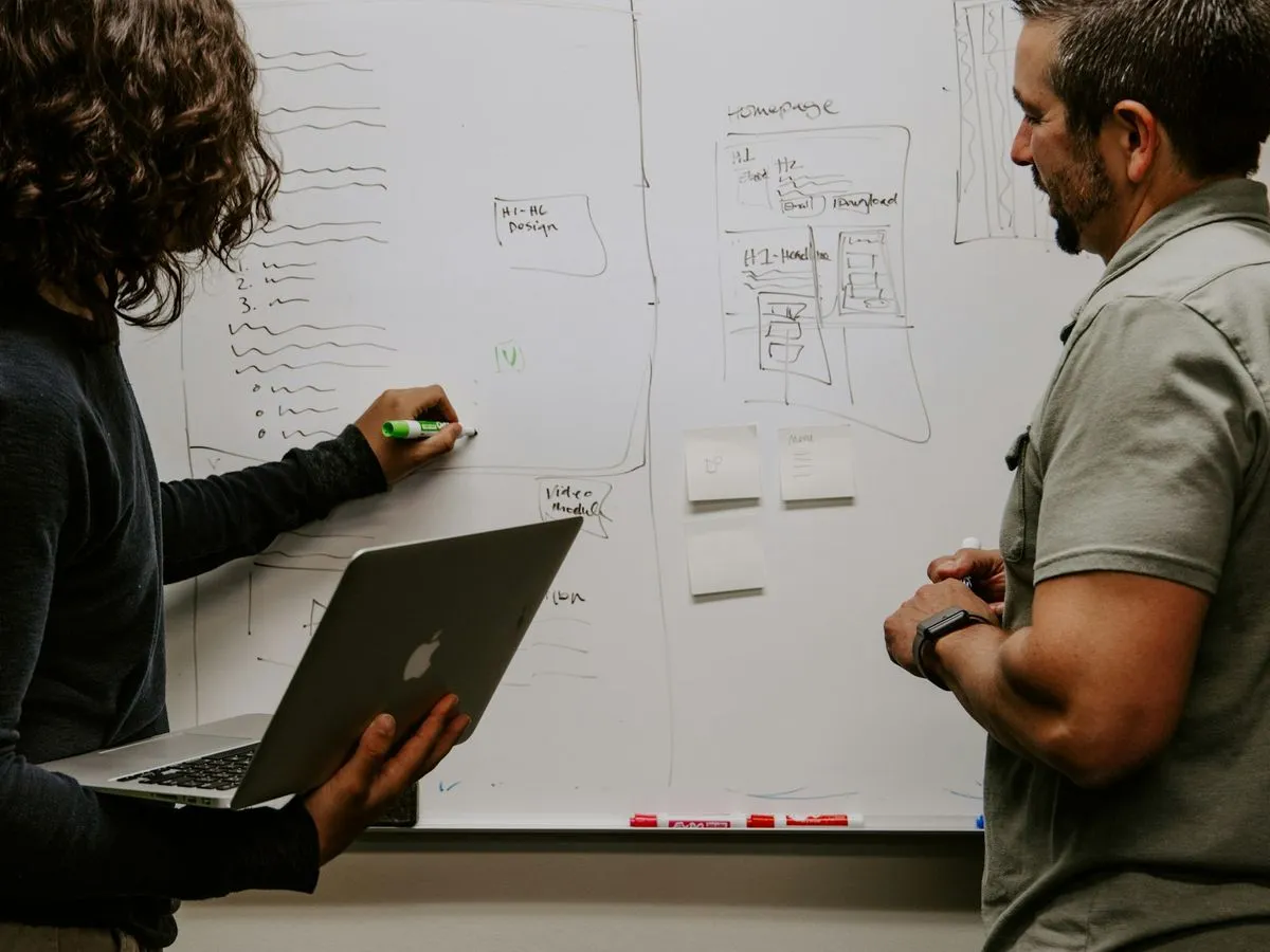 Two colleagues planning at a whiteboard, one holding a laptop